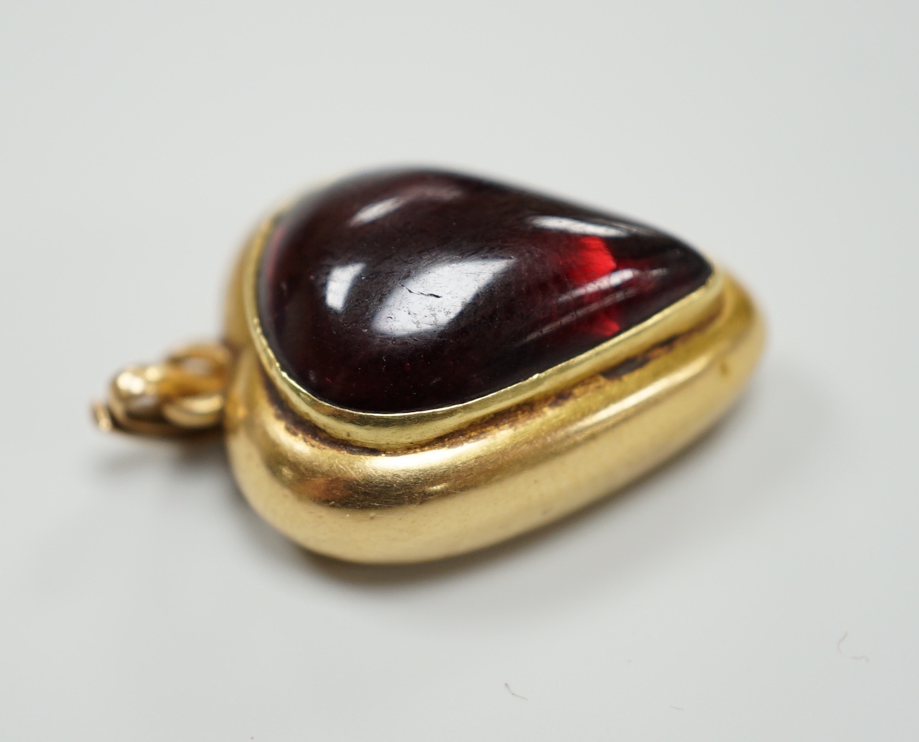 A late Victorian yellow metal (stamped 18) and cabochon garnet set heart shaped pendant, with glazed back, 22mm, gross weight 5.7 grams.